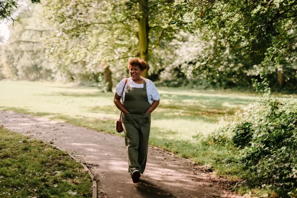 Woman walking briskly on a sunlit park path, a daily habit that helps reduce FUPA fat