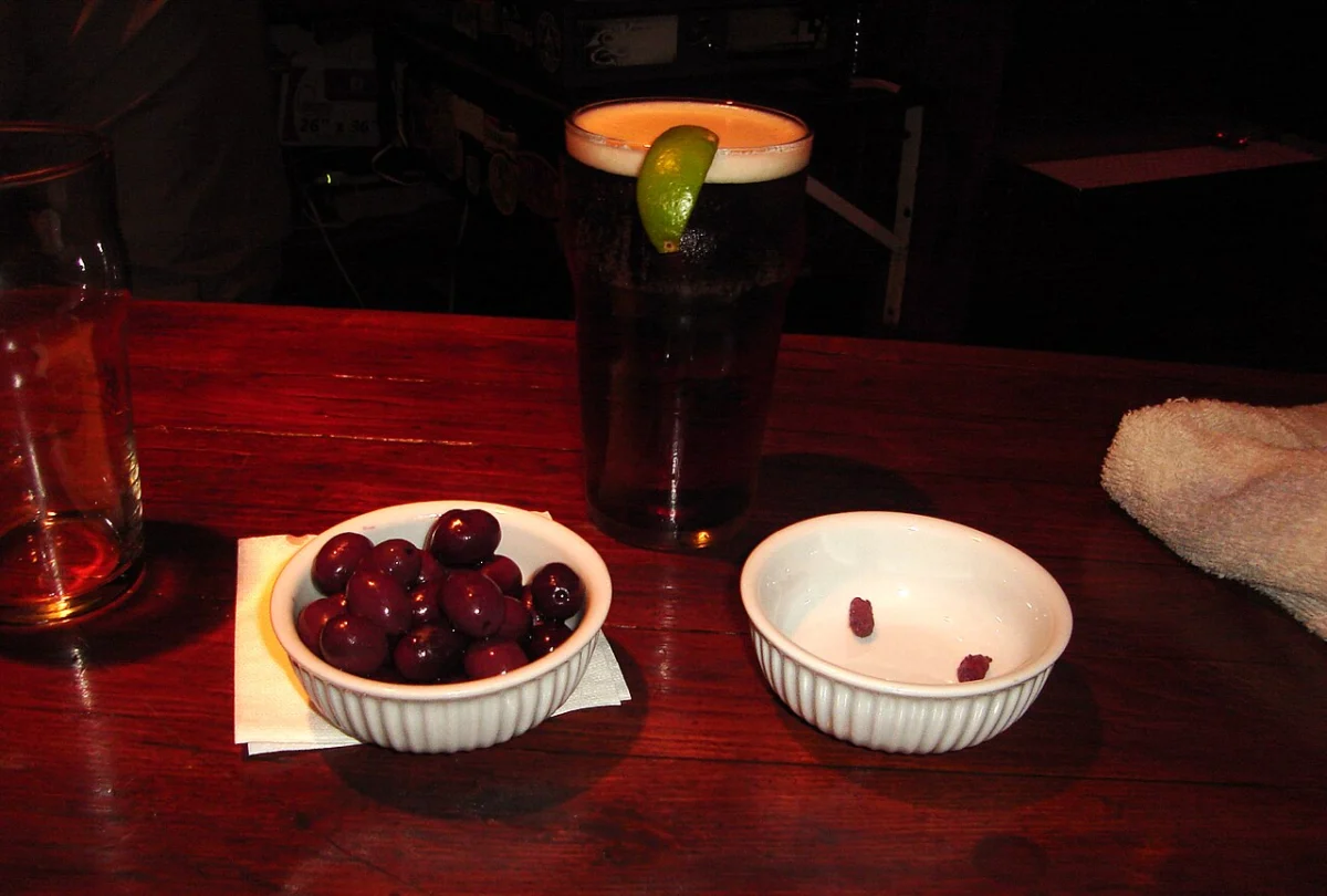 A pint of beer on a pub table next to a bowl of olives, showing how bar snacks add calories while drinking