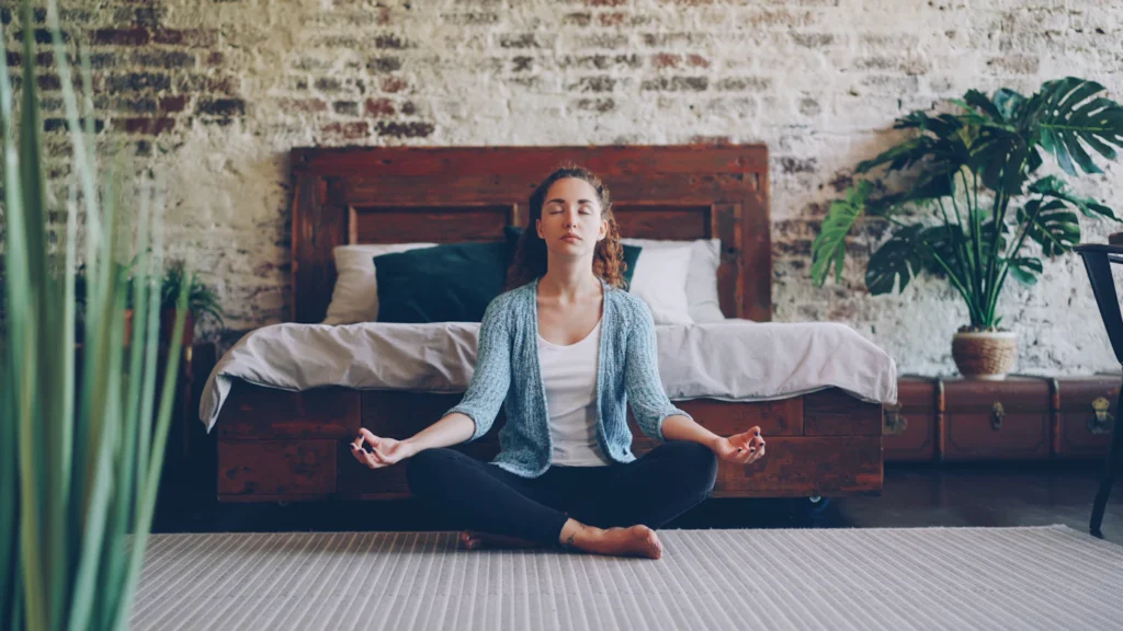 Woman sitting cross-legged on the floor in an upright posture to practise a stomach vacuum