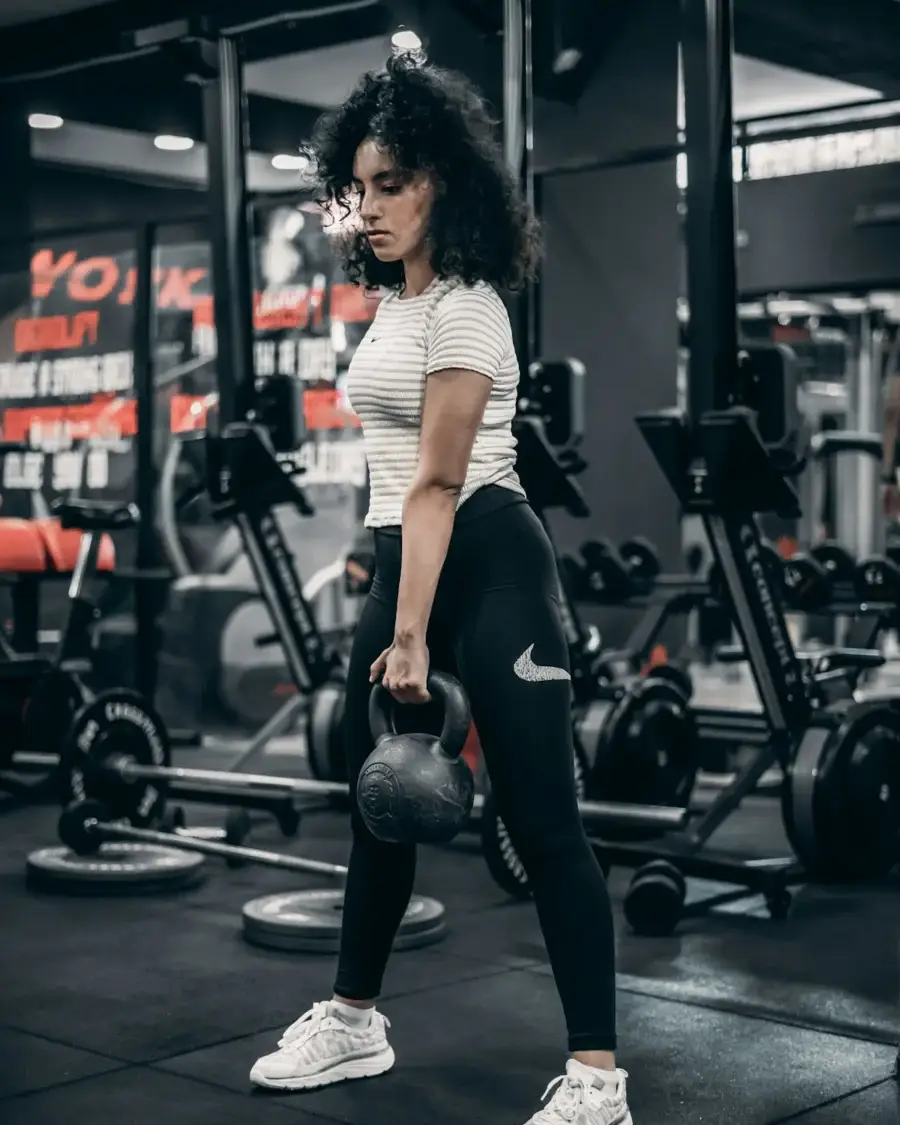 Woman holding a kettlebell in a gym for strength training while losing lower belly fat