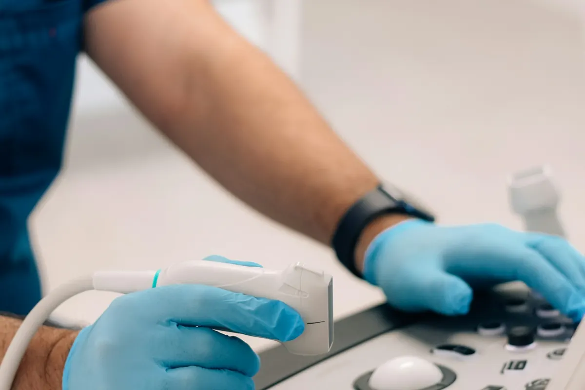 Sonographer's gloved hands on an ultrasound machine, set up to scan a lump in the lower belly