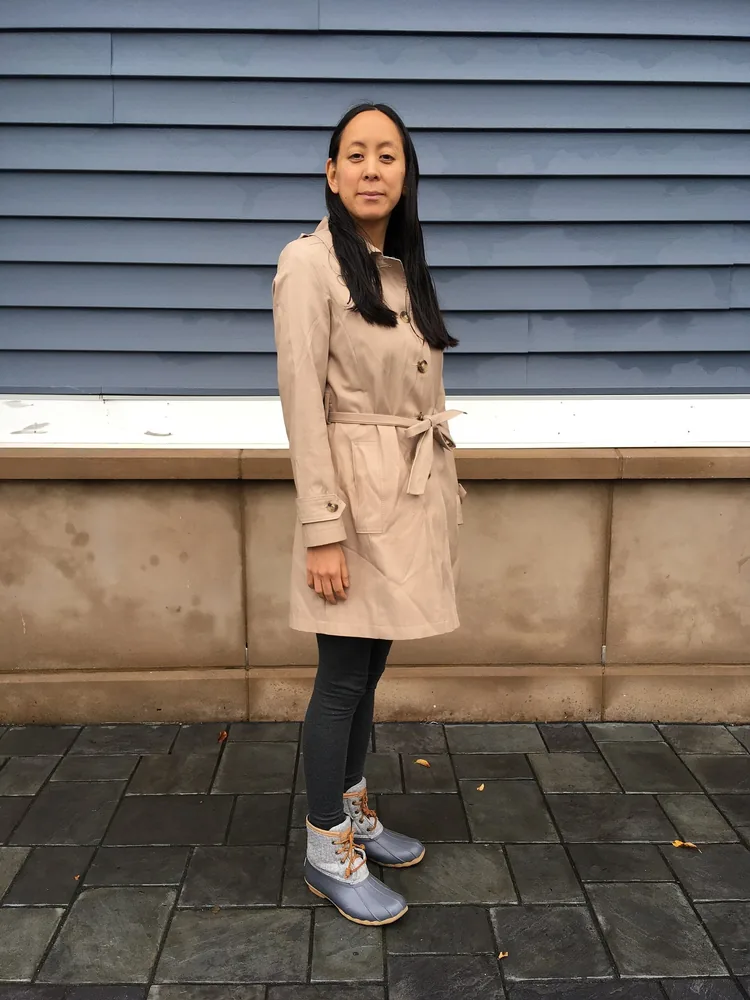 Woman standing outdoors in a beige trench coat tied with a fabric belt at the natural waist